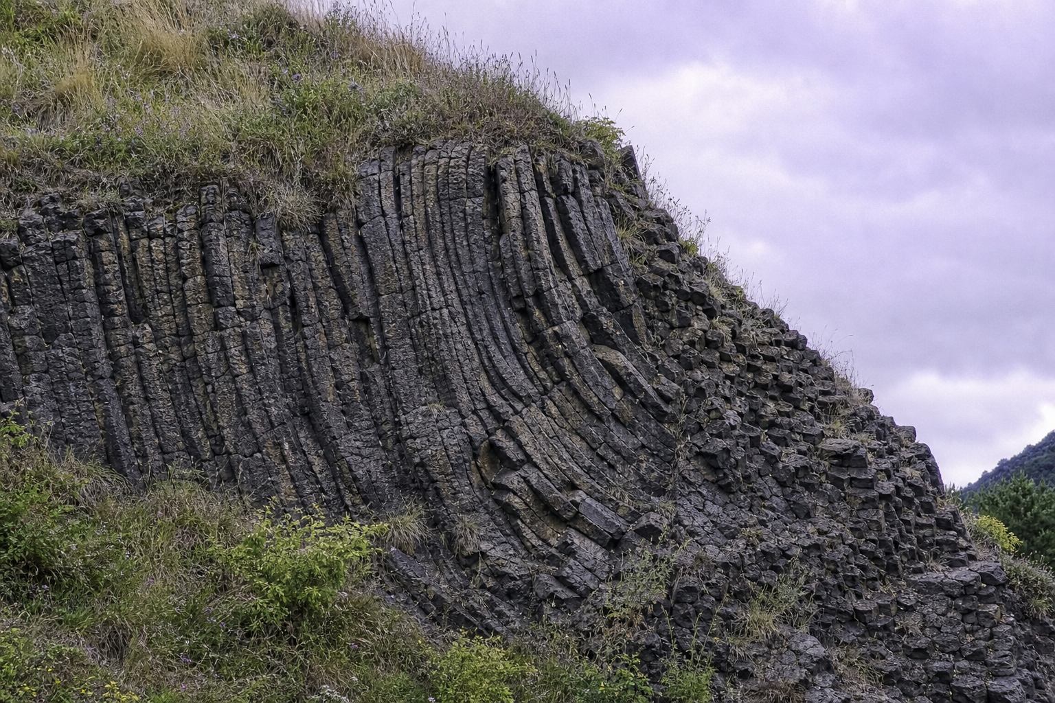 Nahaufnahme dunkler Basaltschichten mit Gras in der Eifel